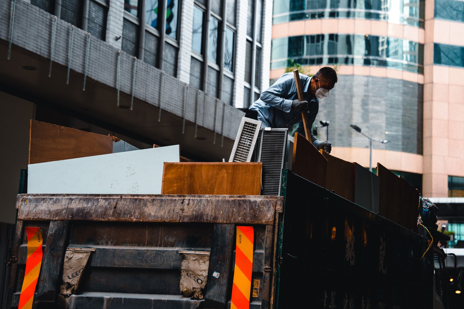 A worker managing construction debris from a large truck in a city environment.